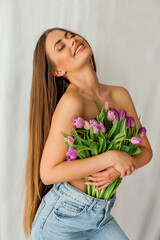 Beautiful young woman with long hair holds bouquet of tulips. Portrait of woman on white background. Spring holidays.