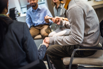 Fototapeta premium Group of people sitting in a circle holding hands and participate in a support meeting. Healthcare and medicine concept.