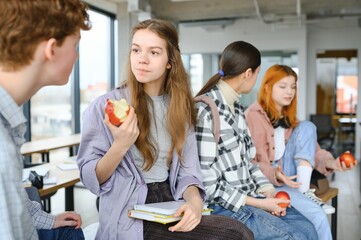 Cheerful students are sitting at desks and eating an apple during a break