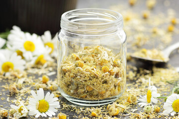 Dried chamomile herbal tea in a jar with flowers on black background, closeup, healing drink,...