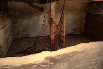 Ein altes Netz hängt von der Decke in einem von Holz umzäunten Raum mit Steinwänden