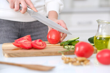 Obraz na płótnie Canvas Woman cutting fresh tomatoes at table in a light kitchen, closeup