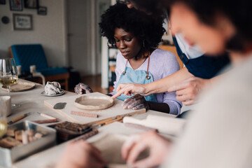 Interracial pottery class student learning with mentor clay modeling.