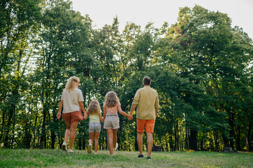 Naklejka na ściany i meble Rear view of family of four walking and exploring nature on sunny summer day.