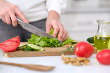 Woman Cutting fresh leaves of salad, tomatoes, cucumbers at table in a light kitchen, closeup
