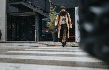 Focused businessman braving snowfall while crossing street in winter.
