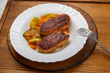 Cutlet with fried vegetables on a white plate on the floor table next to a fork