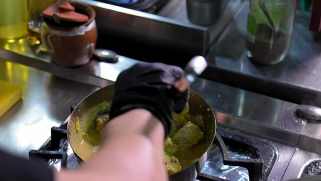 Cooking Satsivi in restaurant kitchen by professional chef traditional Georgian dish of chicken in nut sauce. Hand stirring and adding sauce to pan on gas stove.