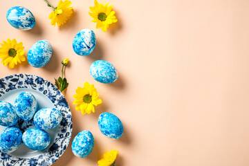 Plate with blue and white Easter eggs and yellow flowers on beige background. Happy Easter concept.