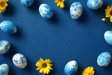 Frame of blue and white Easter eggs and yellow flowers on dark blue background. Top view. Flat lay.