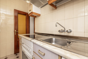 A small kitchen furnished with single wall cabinets, with antique ceramic hob, stainless steel sink with drainer and chrome faucet