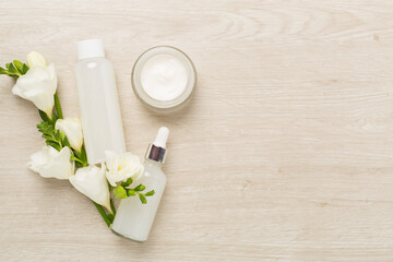 Obraz na płótnie Canvas Facial cosmetic products with freesia flowers on wooden background, top view