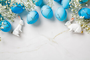 Blue Easter eggs, white flowers, decorative rabbits on marble table.
