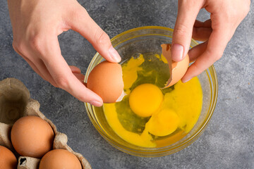 Woman's hands cracking fresh egg, yolk and white dropping in a bowl, top view