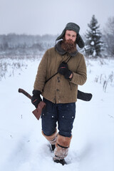 A forester with an ax and a saw walks through the snowy taiga forest, preparing firewood, spruce,...