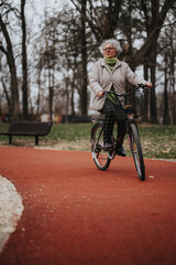 Mature female retiree takes pleasure in a bike ride through a serene park, maintaining fitness and enjoying retirement.