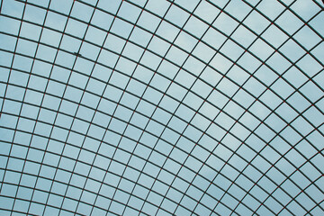 Abstract geometric pattern of a glass ceiling against a clear blue sky.