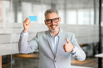 A stylish mature businessman holds up a blank business card, signifying readiness for networking...