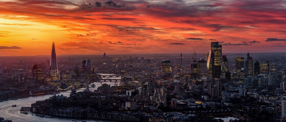 Wide, panoramic view of the urban skyline of London City along the River Thames during a colorful sunset with red and orange clouds, England