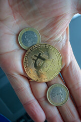 a bitcoin and two euro coins in the palm of my hand
