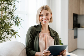 Cheerful caucasian woman looking at camera using digital tablet. Beautiful female girl typing on...