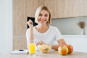 Healthy smiley woman in casual clothes having breakfast looking at camera. Young freelancer taking...