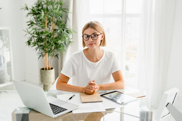Successful caucasian young female student looking at the camera working remotely on laptop....
