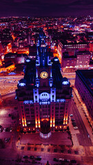 Vertical aerial view of a lit-up cityscape at night with a prominent clock tower and urban streets...