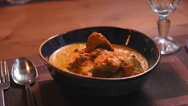 Satsivi is traditional Georgian dish of chicken in walnut sauce in blue plate on table with cutlery and glass in restaurant.