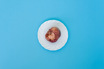 Rotten bitten apple on a saucer, on a blue background, close-up. Studio photo. Advertising/presentation concept.	