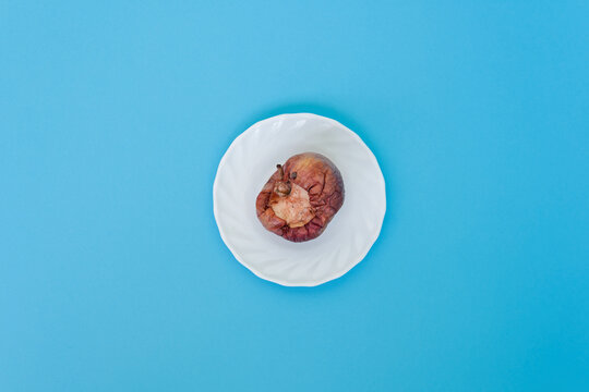 Rotten bitten apple on a saucer, on a blue background, close-up. Studio photo. Advertising/presentation concept.	