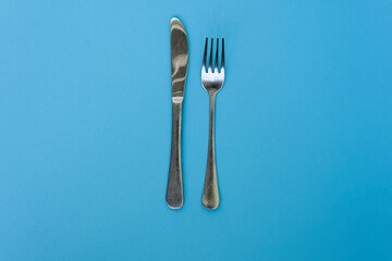 Silver knife and fork isolated on a blue background. Cutlery presentation. Studio photo