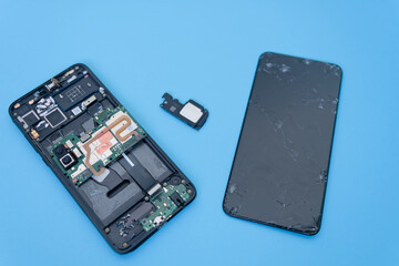 Disassembled components of mobile telephone. Damaged phone screen/display. Blue background....