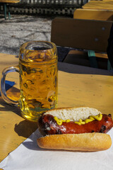 A roasted sausage with bread roll and mustard in a napkin on a beer table in the beer garden next...
