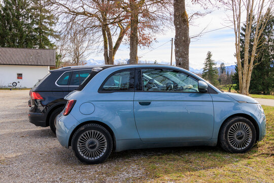 A small blue Fiat 500e convertible next to an SUV in a car park in Uffing am Staffelsee in Germany on 9.3.2024