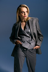 beautiful young woman in fashionable silver suit posing on dark blue backdrop and looking away
