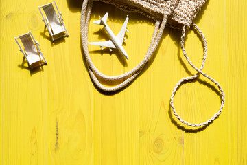 Summer vacation concept with beach bag top view with miniature hammocks and small airplane on yellow wooden planks background with beta visible