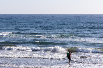 Fototapeta na wymiar Tourist standing in water on a beach taking a photo