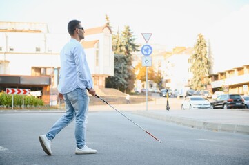 Young handsome blinded man walking with stick in town