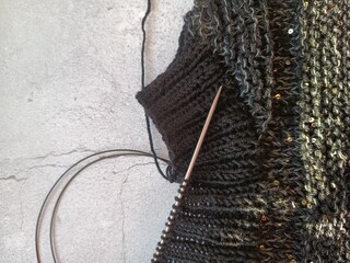 The process of knitting a jumper made of black and gray wool with sequins. High quality photo