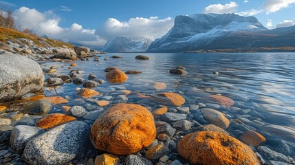 A lake with rocks in the foreground, water ripples, and distant mountains under a clear sky. - obrazy, fototapety, plakaty