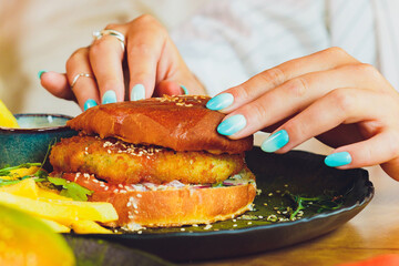 Vegetarian lentil burger in wholewheat bun with lettuce, tomato and cucumber accompanied by French fries Selective Focus, Focus on the front of the sandwich.