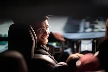 Fotobehang In the nighttime hours, a happy family enjoys playful moments together inside a car as they journey on a nocturnal road trip, illuminated by the glow of headlights and filled with laughter and joy © .shock