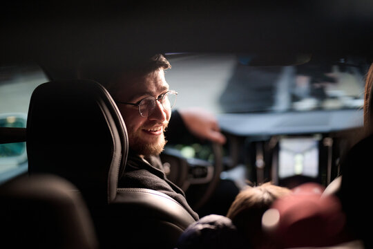 In the nighttime hours, a happy family enjoys playful moments together inside a car as they journey on a nocturnal road trip, illuminated by the glow of headlights and filled with laughter and joy