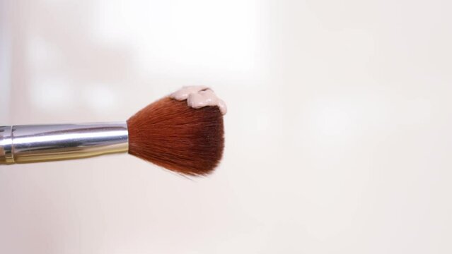 The foundation is poured onto the makeup brush. Decorative cosmetics advertising concept. Brush on a beige background.
