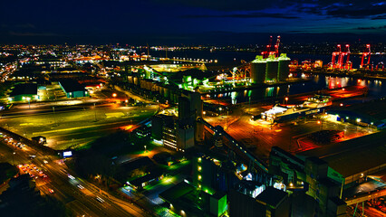 Nighttime aerial view of an industrial port with illuminated cranes and warehouses, showcasing...