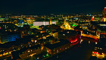 Aerial night view of a vibrant cityscape with illuminated buildings and streets in Leeds, UK.