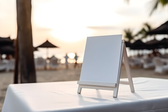 Blank white signboard on table in front of beach at sunset