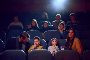 A modern family enjoys quality time together at the cinema, indulging in popcorn while watching a movie with their children