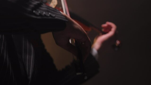 Crop of male hands holding beautiful violin and creating charming tune during performance. Virtuoso musician accompanying opera singer while masterly playing musical instrument on theater stage.